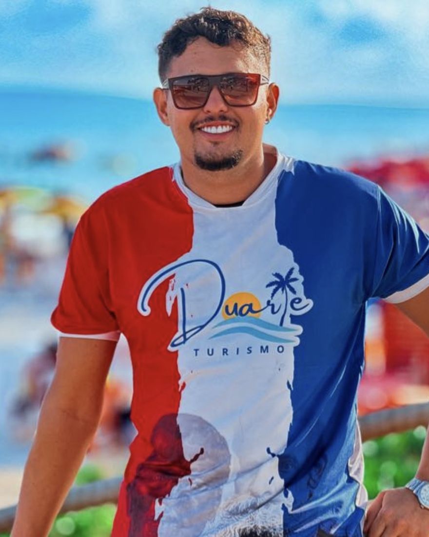 Lucas Duarte sorrindo na praia, com a camisa da Duarte Turismo